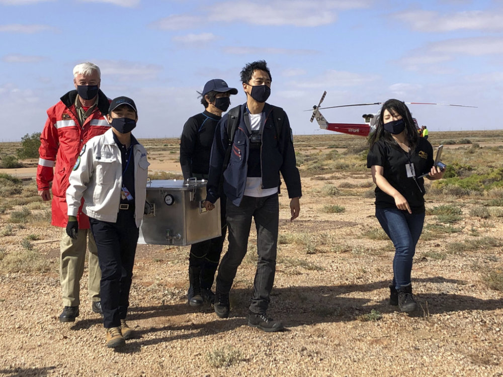 Members of the Japan Aerospace Exploration Agency (JAXA) arrive at a range support facility in Woomera, Australia, on Dec. 6, 2020, carrying a box containing asteroid samples that they retrieved on a remote area in southern Australia. (Australian Space Agency via AP)