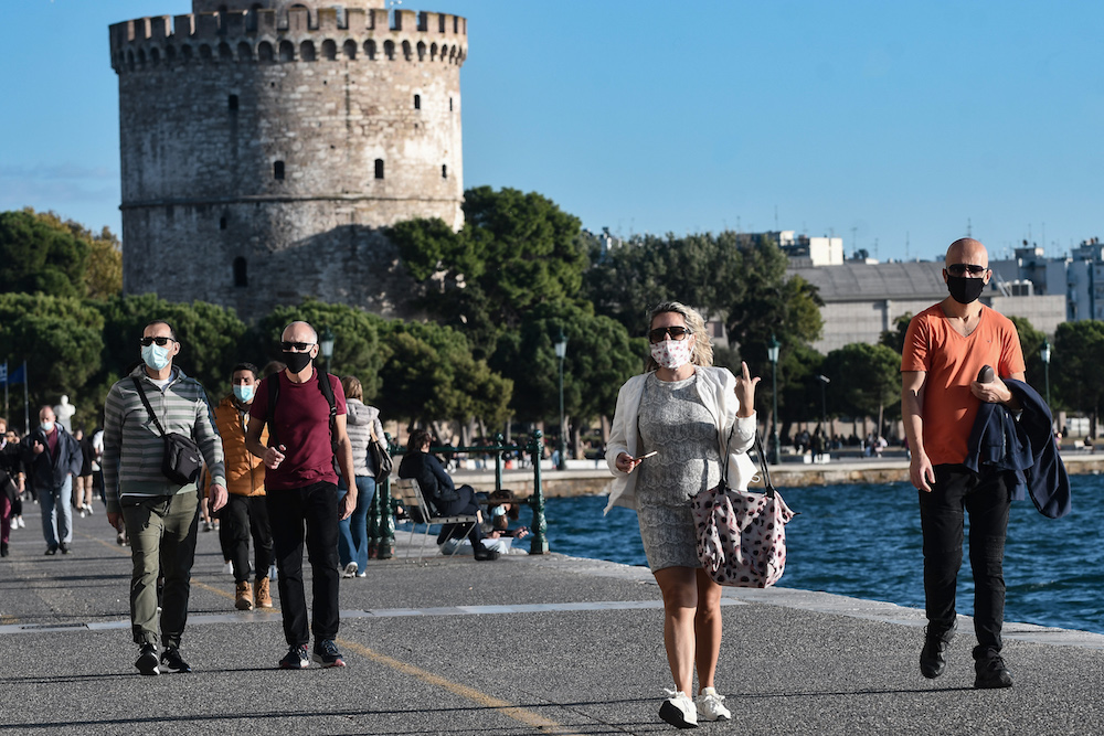 Pedestrians, wearing protective face masks, walk on the waterfront next to the White Tower in Thessaloniki on October 31, 2020, as Greek Prime Minister declared a one-month partial coronavirus lockdown. (AFP/File Photo)