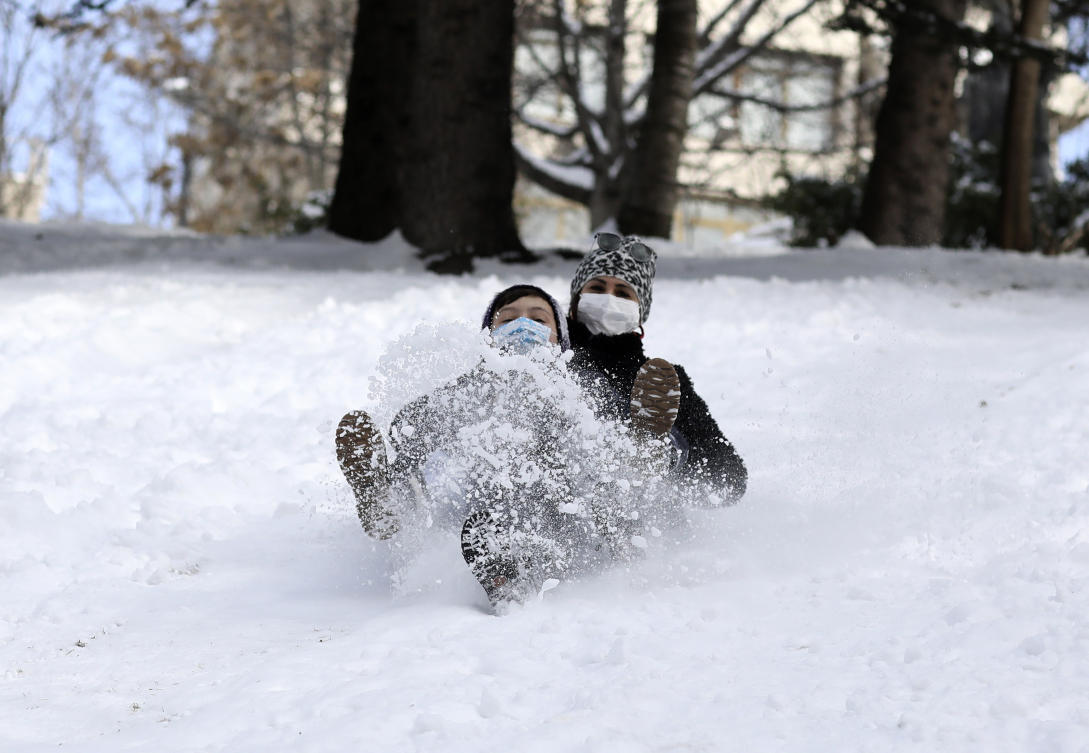 Aysegul Cepoglu, rear, and Ahmet Efe Isik slide down the hill at snow-blanketed Seymenler Park, in Ankara, Turkey, Wednesday, Feb. 17, 2021. (AP)