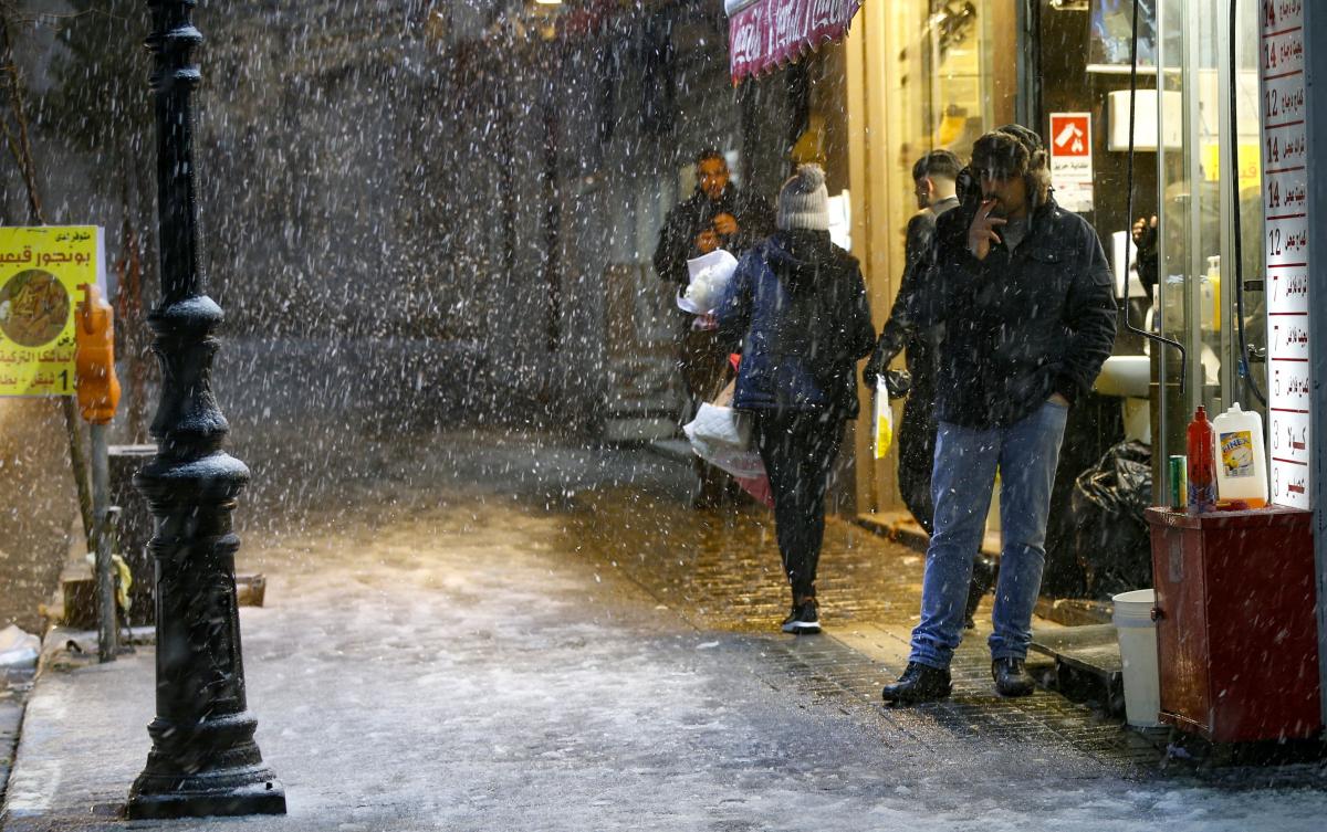 People walk in the street during snowfall in the West Bank city of Ramallah on February 17, 2021. (AFP)