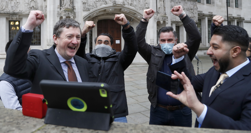 Uber drivers of the (ADCU), App Drivers & Couriers Union, celebrate as they listen to the court decision on a tablet computer outside the Supreme Court in London, Friday, Feb. 19, 2021. (AP)