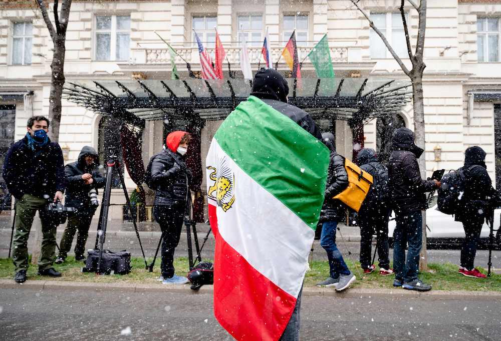 A protester with the Lion and Sun flag of the National Council of Resistance of Iran, an Iranian opposition group, stands in front of the Grand Hotel in Vienna on April 6, 2021, where diplomats of the EU, China, Russia and Iran hold talks. (AFP)