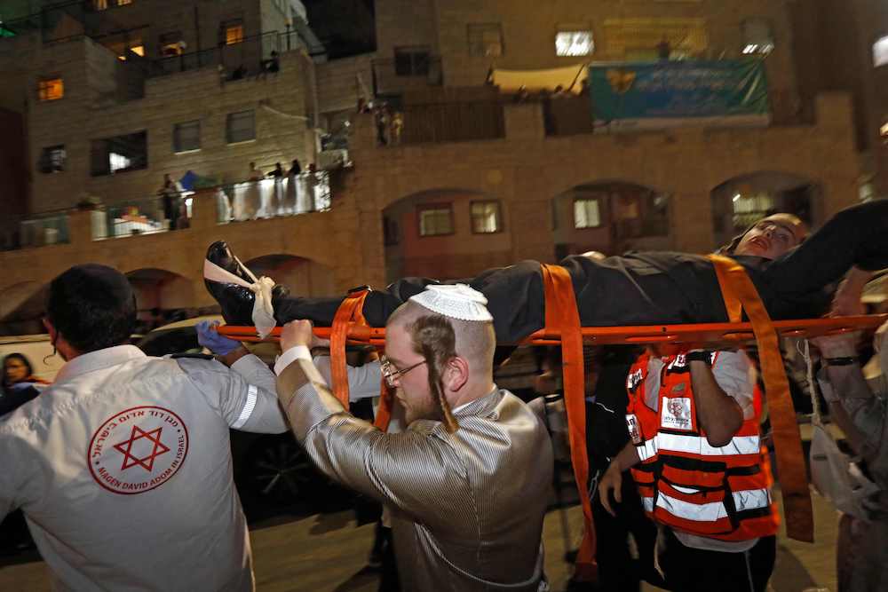 Israeli medics and an ultra-Orthodox Jewish youth evacuate an injured man after the collapse of grandstand seating at a synagogue in the Israeli settlement of Givat Zeev in the occupied West Bank outside Jerusalem, on May 16, 2021. (AFP)