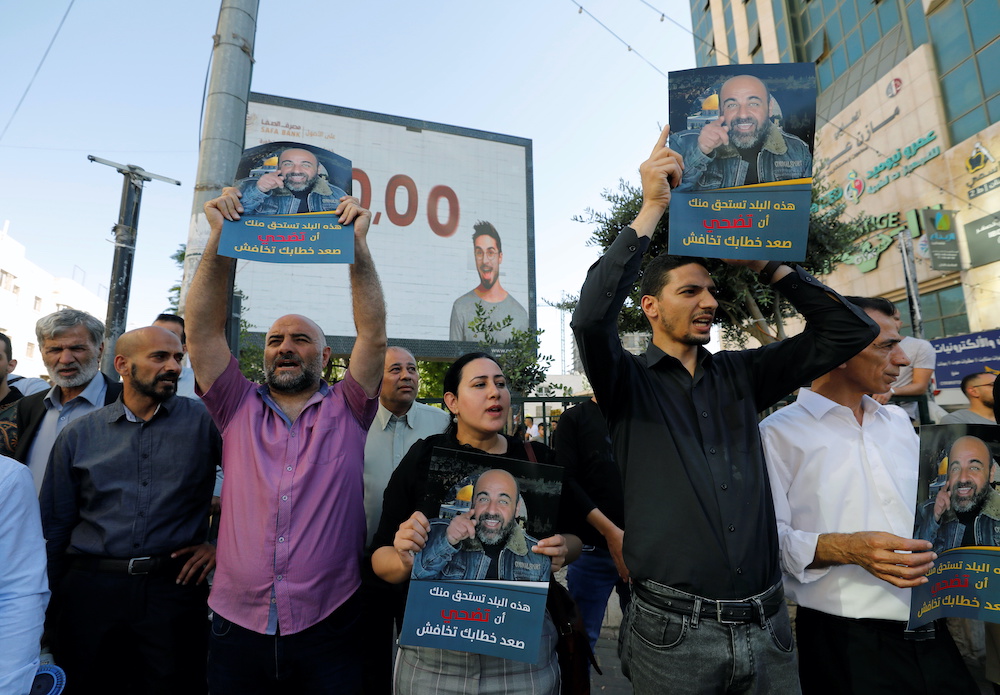 Demonstrators protest over the death of Nizar Banat in the Israeli-occupied West Bank, June 27, 2021. The placard reads, “This country deserves you to sacrifice, raise your voice and don’t be afraid.” (Reuters)