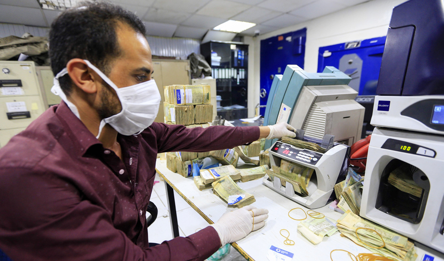 An employee wearing a face mask and gloves counts local currency at a bank in the Yemeni capital Sanaa. (AFP file photo)