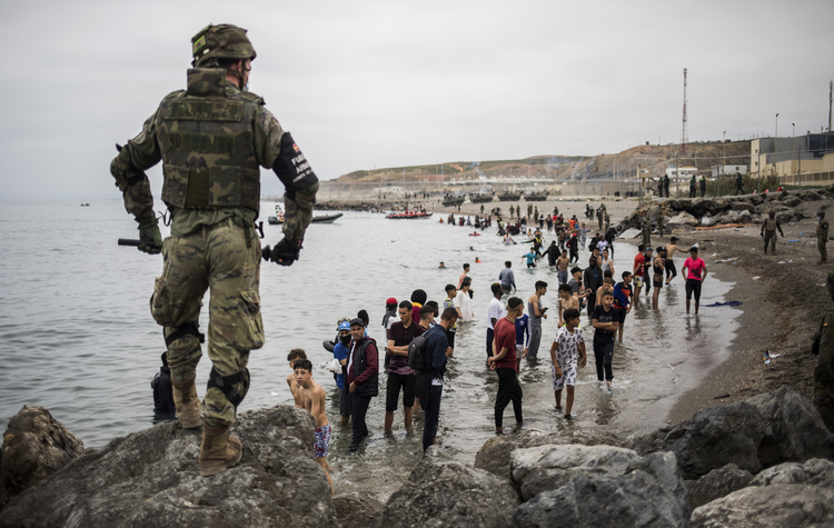 People mainly from Morocco stand on the shore as the Spanish Army cordons off a beach at the border of Morocco and Spain in the Spanish enclave of Ceuta on May 18. (AP/File Photo)