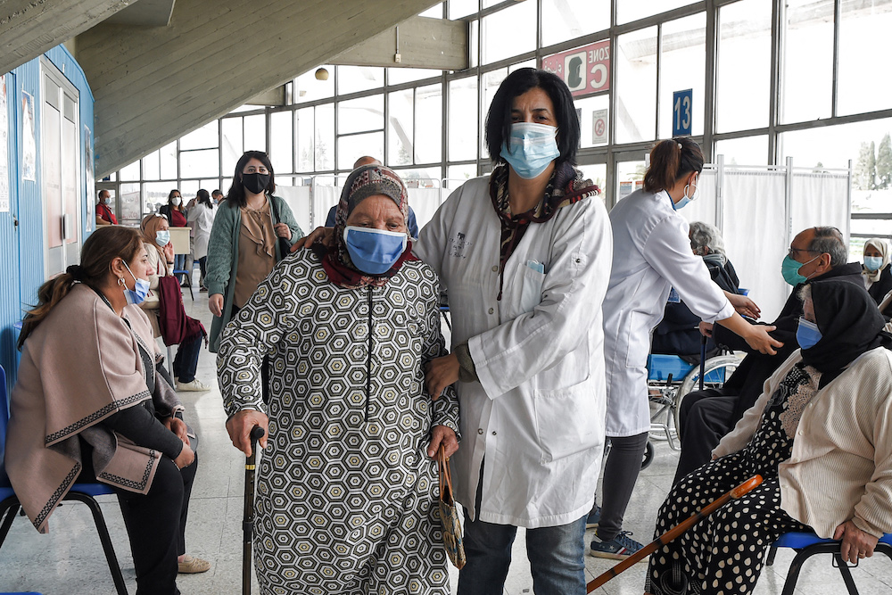 A medical worker assists an elderly woman arriving to receive a dose of the Pfizer-BioNTech COVID-19 coronavirus vaccine at El-Menzah sports hall in Tunisia's capital Tunis. (AFP/File Photo)