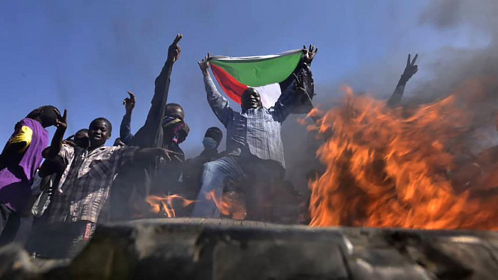 A man holds a Sudanese national flag before flames at a barricade as people protest against the military coup in Sudan, in "Street 60" in the east of capital Khartoum on November 13, 2021. (AFP)