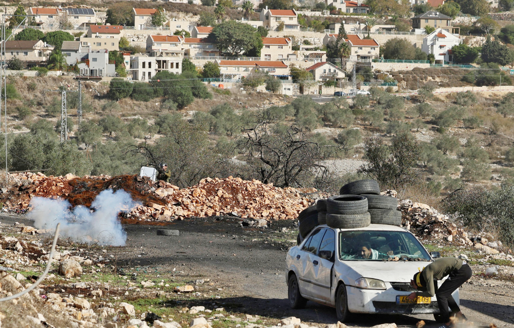 Palestinian protesters use a car for shelter as Israeli security forces fire tear gas during clashes in the village of Kfar Qaddum in the occupied West Bank on December 10, 2021. (AFP)