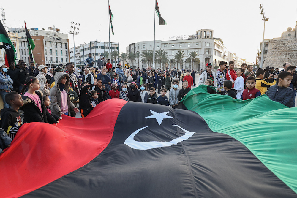 Children wave a giant Libyan national flag as people gather at the Martyrs’ Square in the center of Libya’s capital Tripoli on Dec. 24, 2021, to mark the country’s 70th independence day. (AFP)