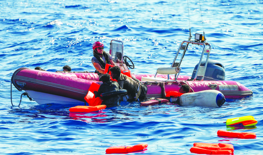 An NGO crew member helps migrants to get onboard after their wooden boat overturned during a rescue operation at the Mediterranean Sea. (AP)