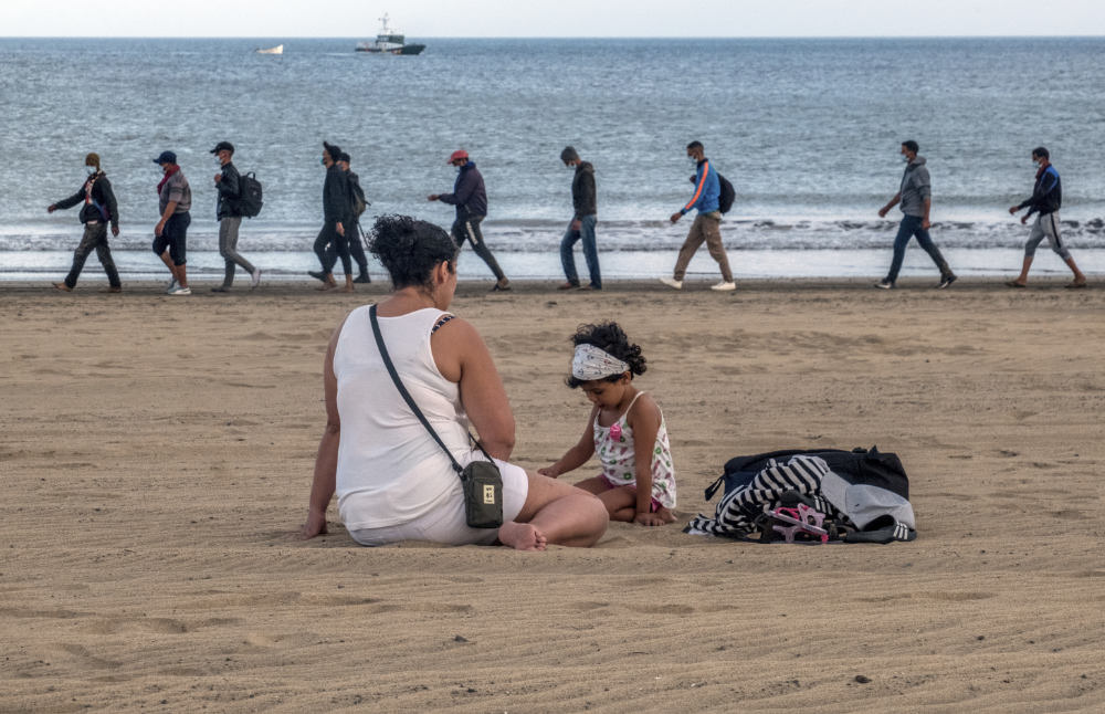 Migrants from Morocco walk along the shore escorted by Spanish Police after arriving at the coast of the Canary Island, crossing the Atlantic Ocean sailing on a wooden boat on Oct.20, 2020. (AP)