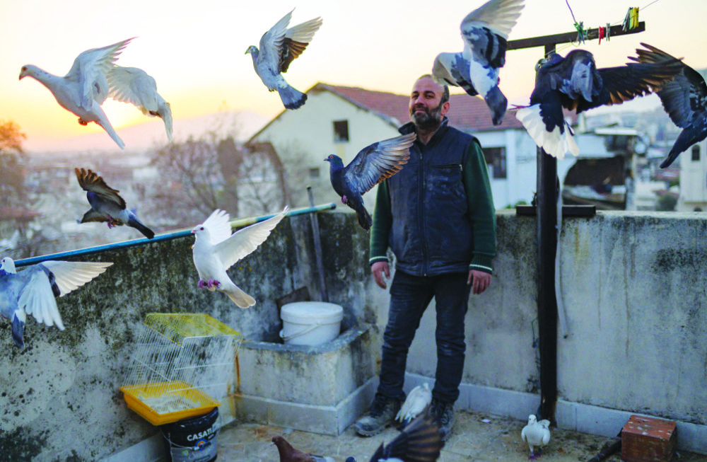 Murat Guzel scatters bird food on the roof of a restaurant where he worked before the earthquake in Antakya. (AFP)