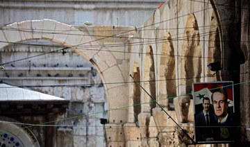 A poster depicting Syria's President Bashar al-Assad and his father and predecessor Hafez al-Assad hangs along an alley in Damascus on April 21, 2021. (AFP/LOUAI BESHARA)