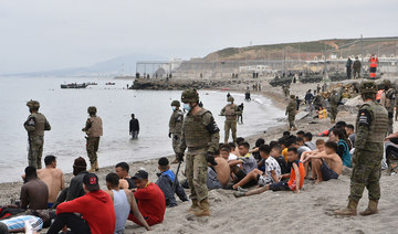 Migrants, including minors, who arrived swimming at the Spanish enclave of Ceuta, rest as Spanish soldiers stand guard on May 18, 2021 in Ceuta. (AFP)