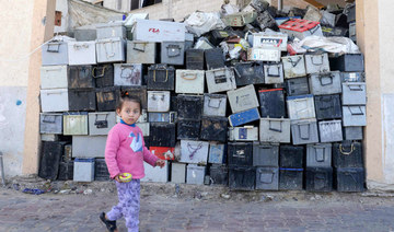 A Palestinian girl walks past a stack of discarded batteries slated for recycling in Khan Yunis in the southern Gaza Strip, on February 14, 2022. (AFP)