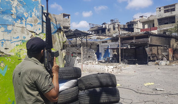 A member of the Palestinian Fatah group stands guard in front of houses riddled with bullets after deadly clashes.