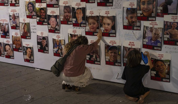 An Israeli woman touches photos of Israelis missing and held captive in Gaza, displayed on a wall in Tel Aviv. (AP)