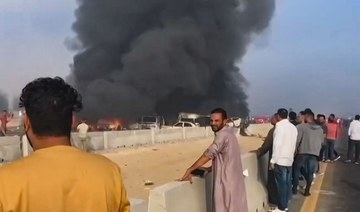 People watch as black smoke billows from charred vehicles following a collision on the Cairo-Alexandria desert road.