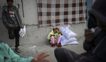 A displaced Palestinian girl sits next to sacks of humanitarian aid at the UNRWA distribution center in Rafah, Gaza.