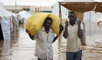 Displaced Sudanese men look on as they carry sacks through a flooded street near the UNHCR tents, following a heavy rainfall.