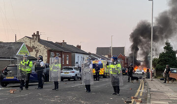 Smoke billows from a fire started by protesters as police stand guard after disturbances near Southport Islamic Society Mosque