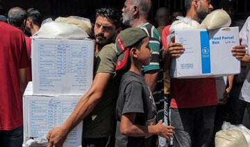 People receive humanitarian aid packages provided by UNRWA from a warehouse in central Gaza City on August 27, 2024. (AFP)