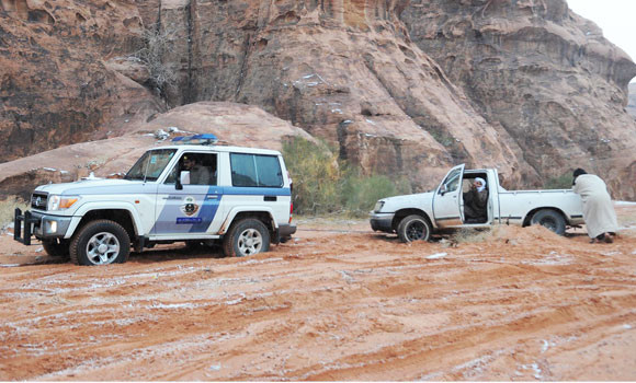 A police vehicle pulls a pickup truck as it gets stuck in mud in Tabuk ...