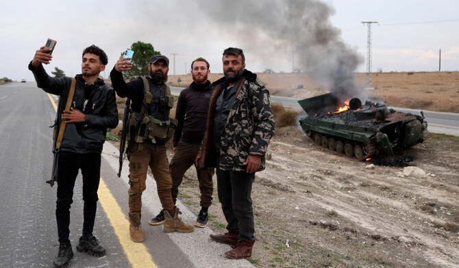 Armed men pose for pictures near a military vehicle belonging to the Syrian forces and seized by anti government forces, on fire after it was hit by government forces, in the Hama governorate, on December 7, 2024. (AFP)