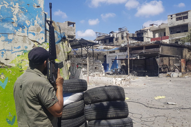 A member of the Palestinian Fatah group stands guard in front of houses riddled with bullets after deadly clashes.