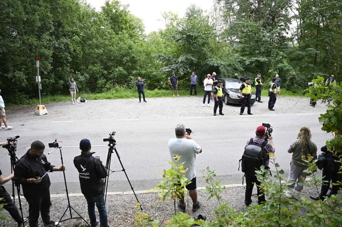 Iraqi refugee in Sweden Salwan Momika (back, L) holds a Qur’an as policemen and journalists stand around him during a protest.