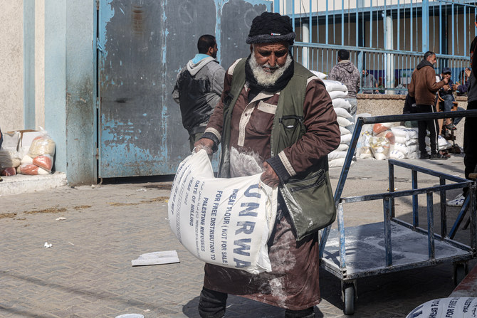 Palestinians carry bags of flour received as aid to poor families, at the UNRWA distribution center, in the Rafah refugee camp.