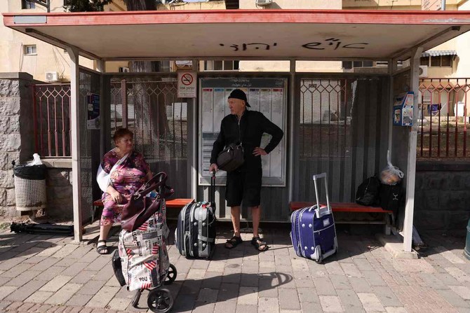 People with their luggage wait at a bus stop in the northern Israeli town of Kiryat Shmona on the border with Lebanon.