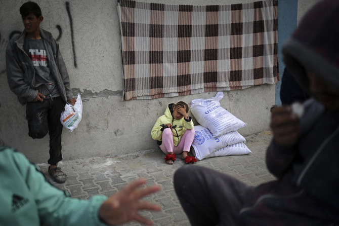 A displaced Palestinian girl sits next to sacks of humanitarian aid at the UNRWA distribution center in Rafah, Gaza.