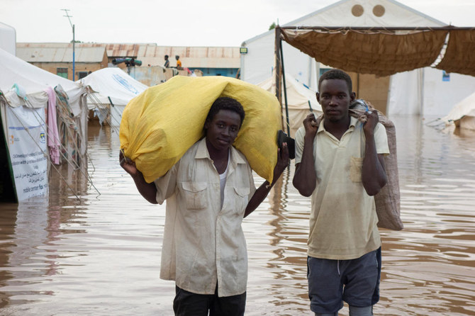 Displaced Sudanese men look on as they carry sacks through a flooded street near the UNHCR tents, following a heavy rainfall.