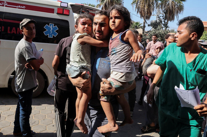 A Palestinian man carries children wounded in an Israeli strike at Al-Aqsa Martyrs Hospital in Deir Al-Balah.