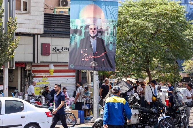 People walk past a banner featuring a picture of the late Hamas political leader Ismail Haniyeh.