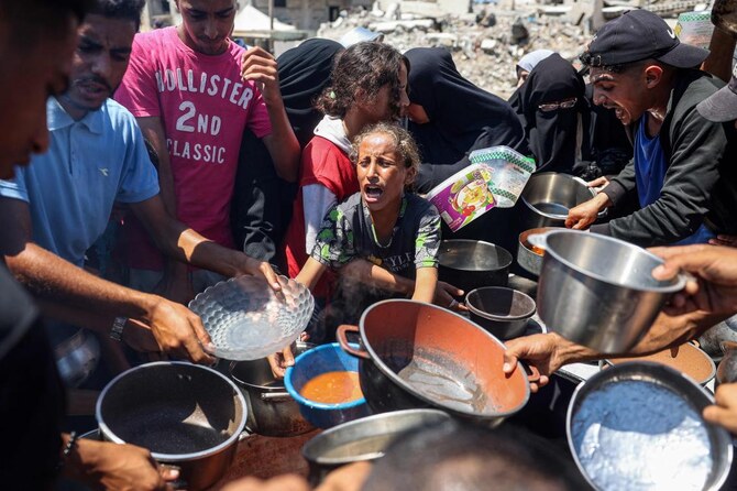 A child reacts as people gather to receive meals during food distribution from a kitchen in the Bureij camp for refugees. 