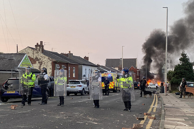 Smoke billows from a fire started by protesters as police stand guard after disturbances near Southport Islamic Society Mosque