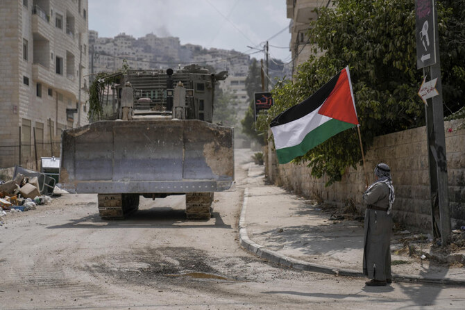 A man waves the Palestinian flag as a convoy of Israeli military bulldozers drive by during an army raid in Jenin, West Bank.