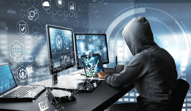 Side view of hacker using computer with digital interface while sitting at desk of blurry interior. (Shutterstock)